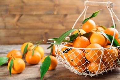 Photo of Fresh ripe tangerines with green leaves on wooden table, closeup