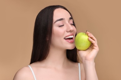 Beautiful young woman with apple on beige background