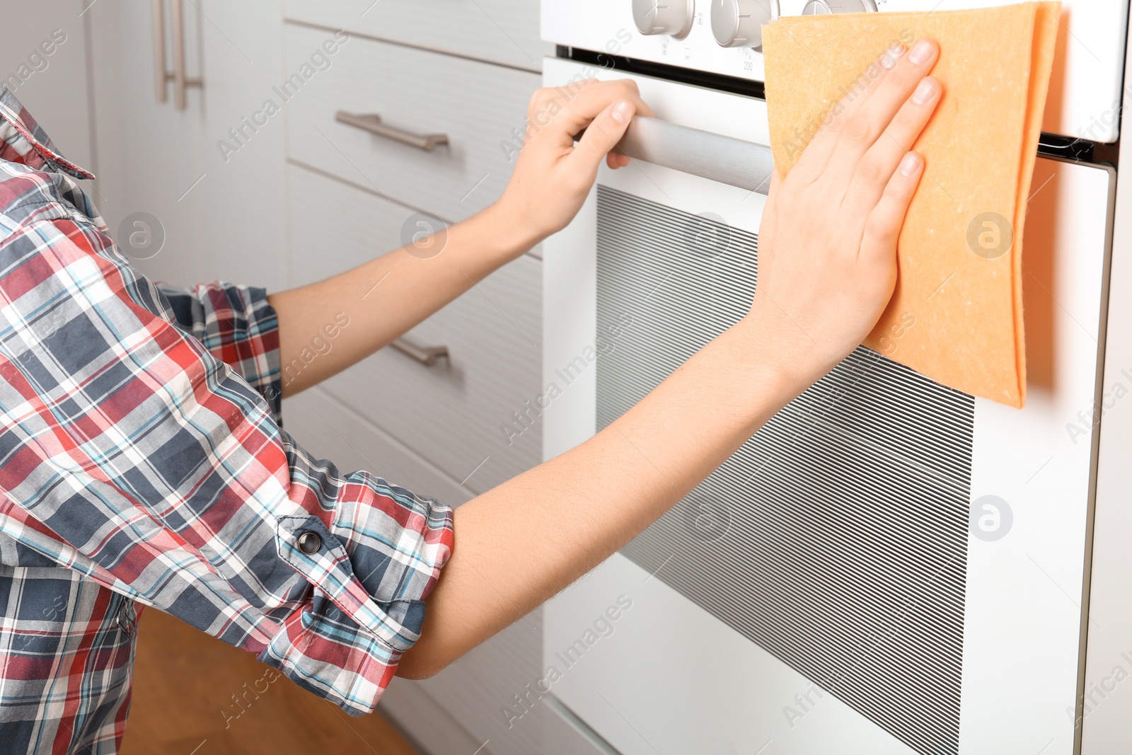 Photo of Woman cleaning electric oven with rag in kitchen, closeup