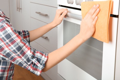 Woman cleaning electric oven with rag in kitchen, closeup