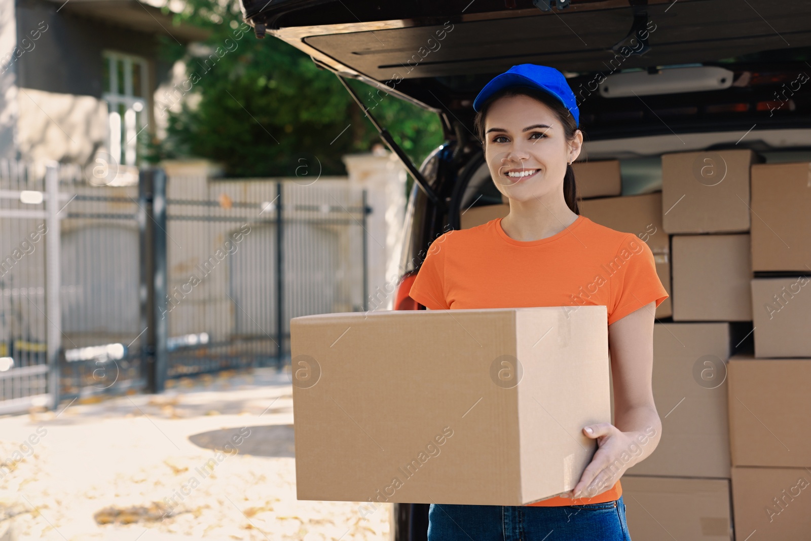 Photo of Courier holding package near delivery truck outdoors, space for text