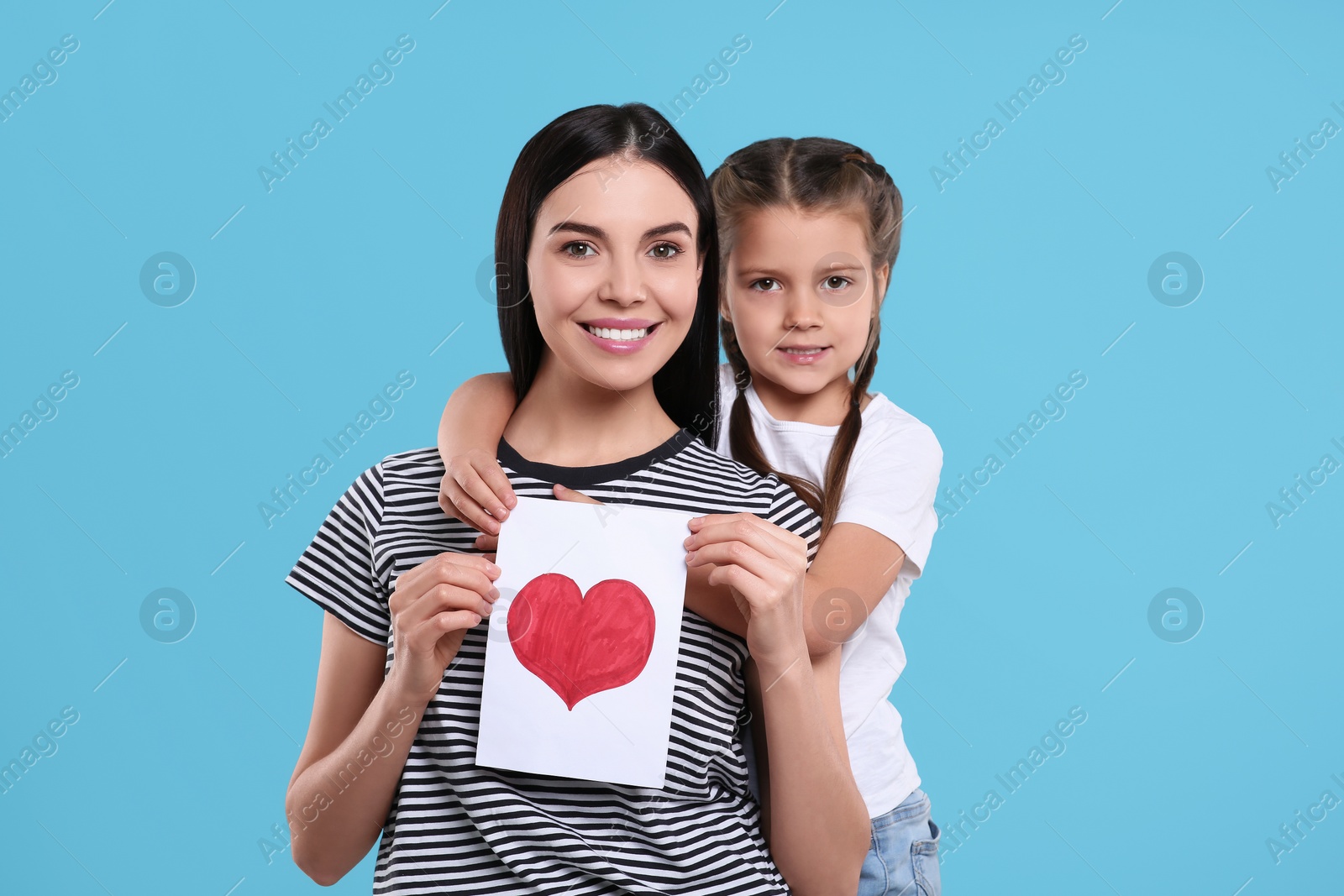 Photo of Happy woman with her cute daughter and handmade greeting card on light blue background. Mother's day celebration