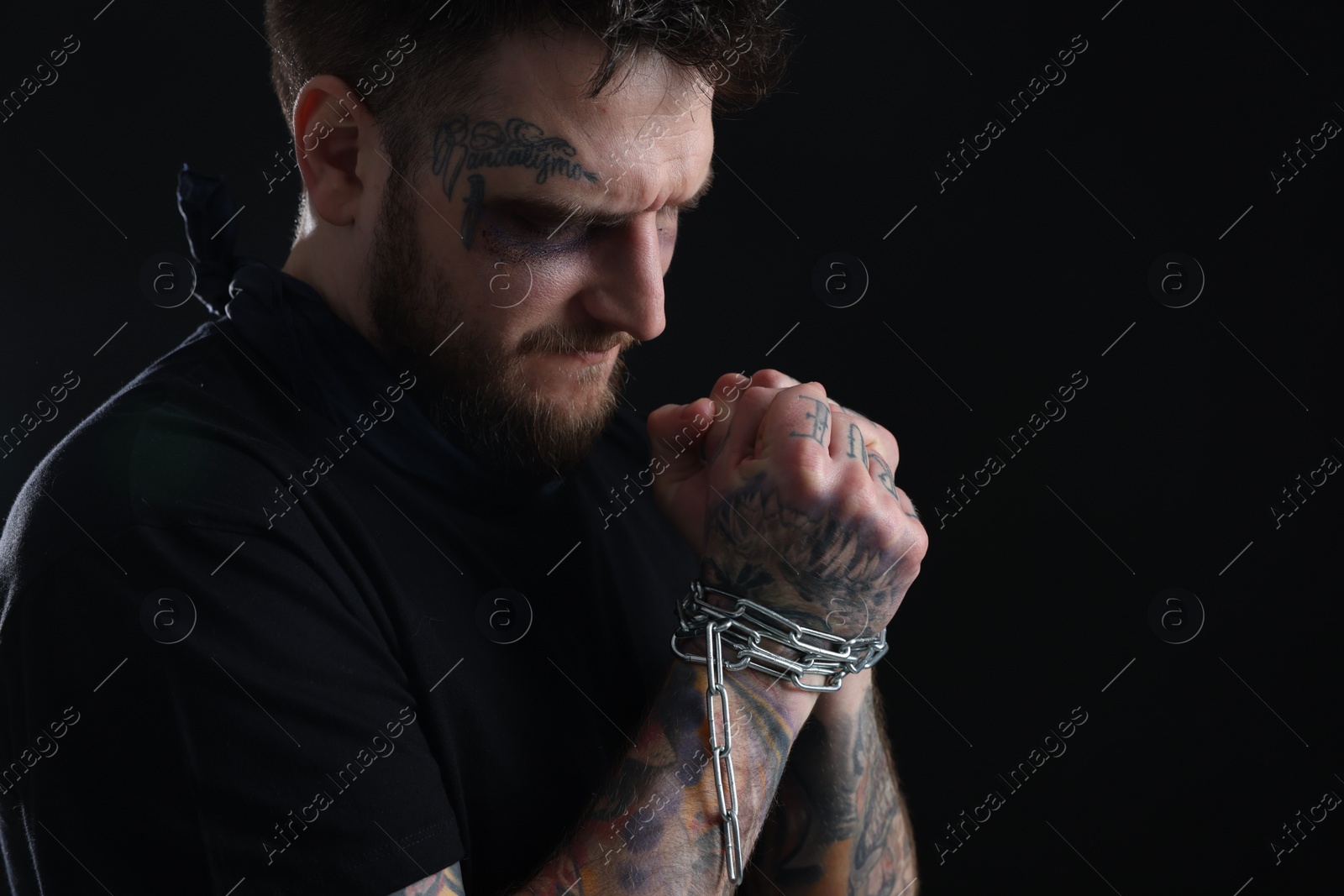Photo of Man with bruise chained on dark background, space for text. Hostage