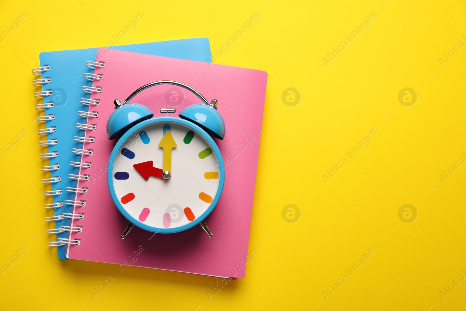 Photo of Alarm clock and notebooks on yellow background, top view. Space for text