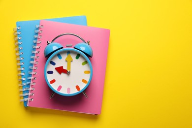 Alarm clock and notebooks on yellow background, top view. Space for text