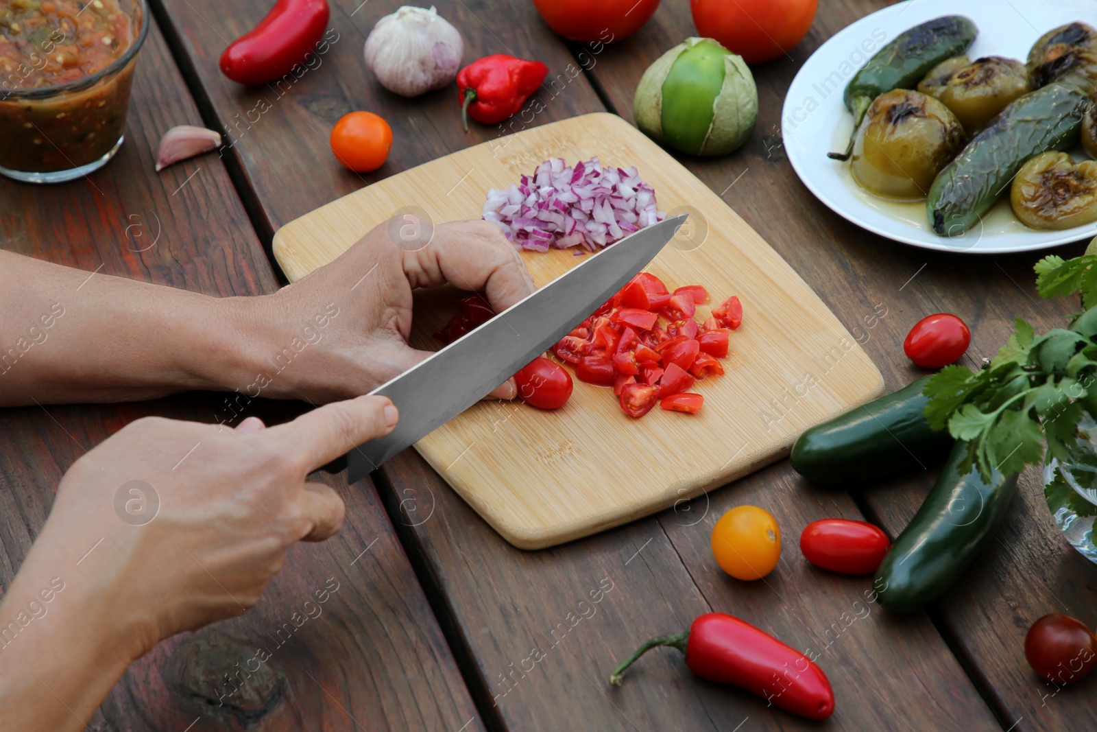 Photo of Woman cutting tomato for salsa sauce at wooden table, closeup