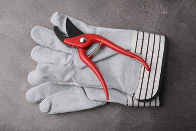 Pair of gardening gloves and secateurs on grey table, top view