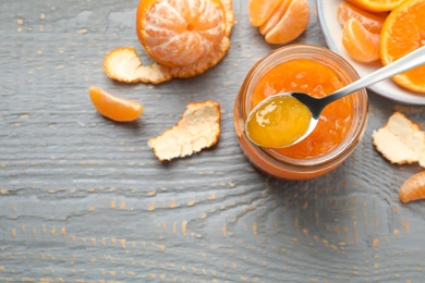 Flat lay composition with tasty tangerine jam on grey wooden table. Space for text