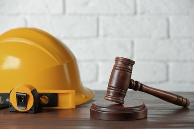 Photo of Construction and land law concepts. Judge gavel, protective helmet, level with tape measure on wooden table, space for text