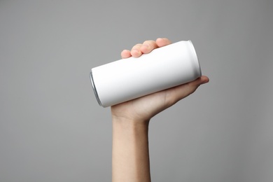 Woman holding aluminum can with beverage on grey background, closeup. Space for design