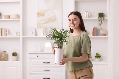 Beautiful young woman with green houseplant at home, space for text