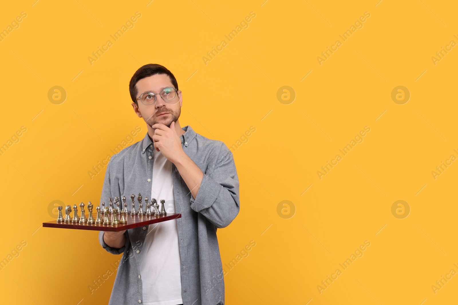 Photo of Thoughtful man holding chessboard with game pieces on orange background. Space for text