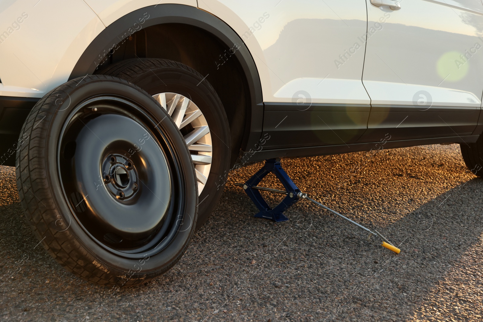 Photo of Car lifted by scissor jack and spare wheel on roadside