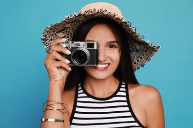 Photo of Beautiful young woman with straw hat and camera on light blue background