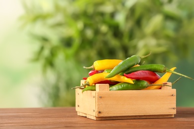 Photo of Crate with chili peppers on table against blurred background