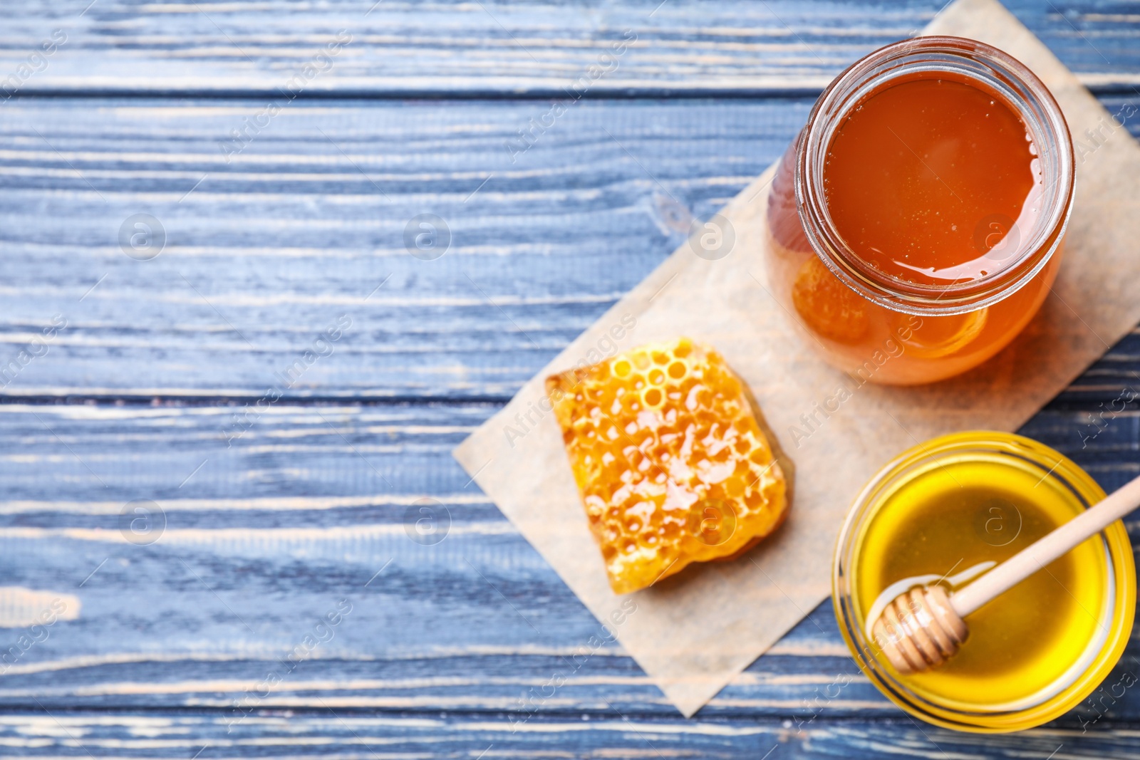 Photo of Tasty honey on blue wooden table, flat lay. Space for text