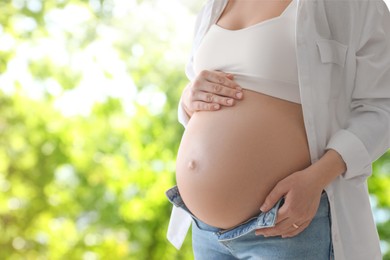 Young pregnant woman touching her belly outdoors, closeup. Space for text