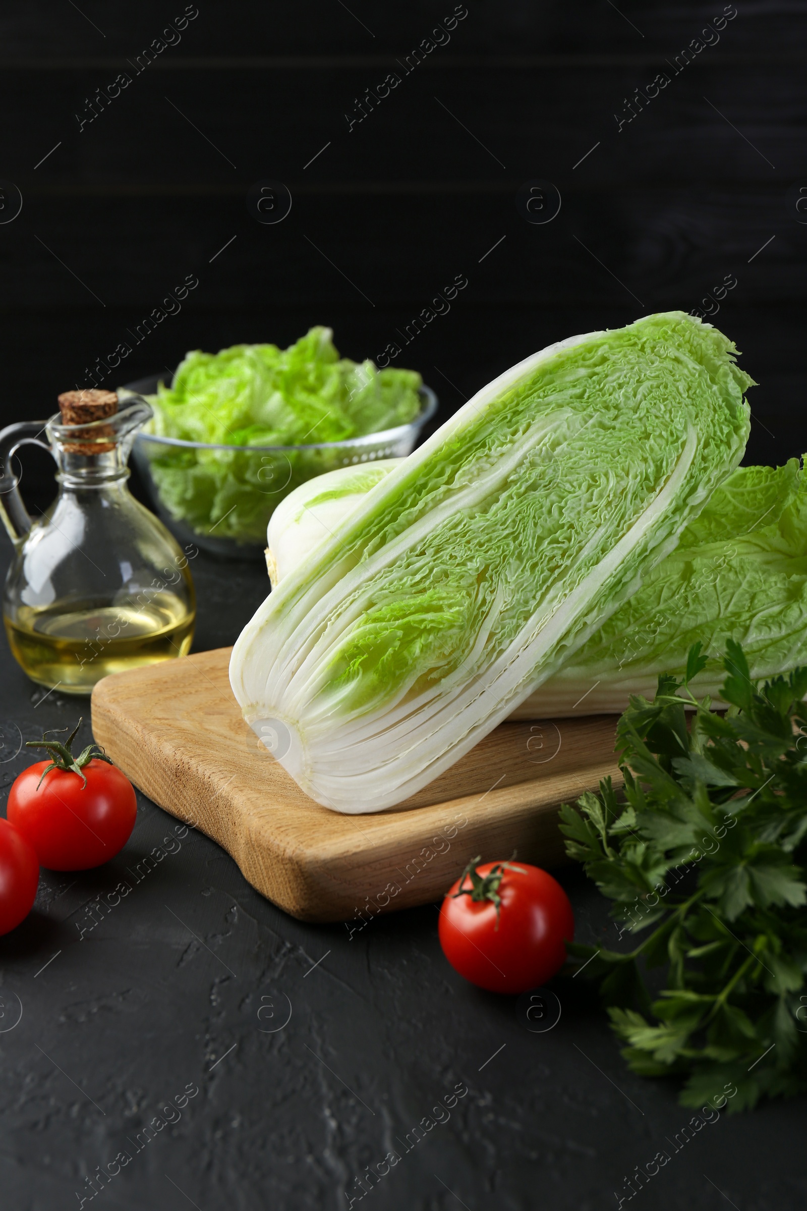 Photo of Fresh Chinese cabbages, tomatoes, parsley and oil on black textured table