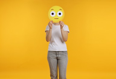 Photo of Woman covering face with surprised emoticon on yellow background