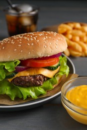 Photo of Delicious burger, soda drink and french fries served on grey wooden table, closeup