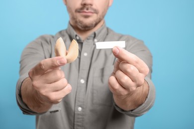 Photo of Man holding tasty fortune cookie with prediction on light blue background, closeup