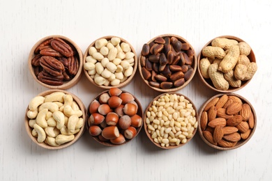 Photo of Bowls with different organic nuts on white wooden background, top view. Snack mix