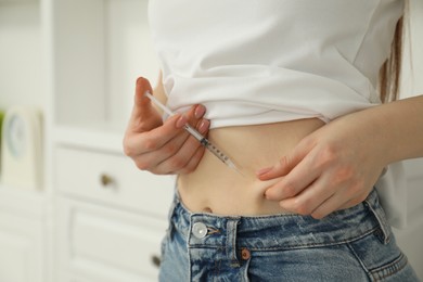 Photo of Diabetes. Woman making insulin injection into her belly indoors, closeup