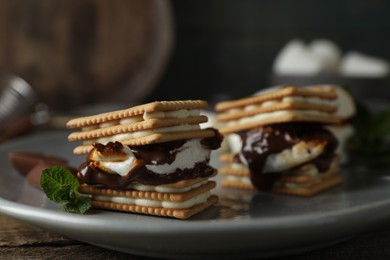 Photo of Delicious marshmallow sandwiches with crackers and chocolate on grey plate, closeup