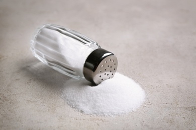 Photo of Scattered salt and shaker on light grey table, closeup