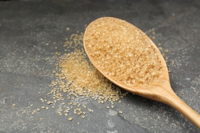 Photo of Spoon with brown sugar on grey textured table, closeup