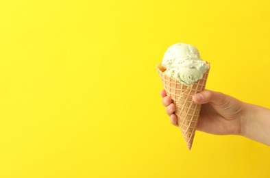 Woman holding waffle cone with delicious ice cream on yellow background, closeup. Space for text