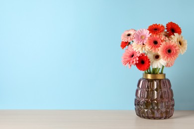 Photo of Bouquet of beautiful colorful gerbera flowers in vase on table against light blue background. Space for text