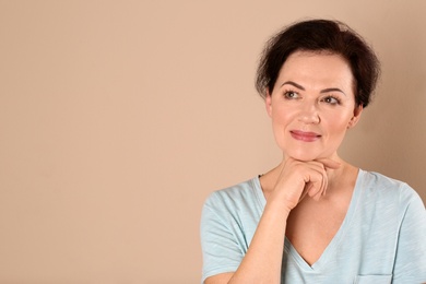 Portrait of charming mature woman with healthy beautiful face skin and natural makeup on beige background, space for text