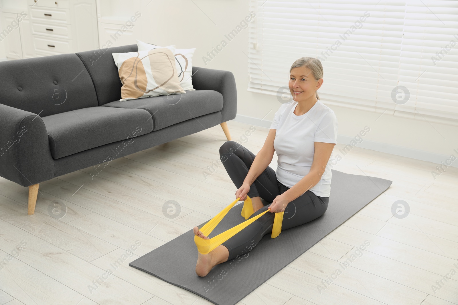 Photo of Senior woman doing exercise with fitness elastic band on mat at home