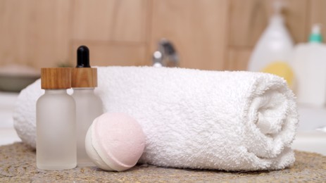 Photo of Rolled bath towel and different cosmetic products on table in bathroom, closeup