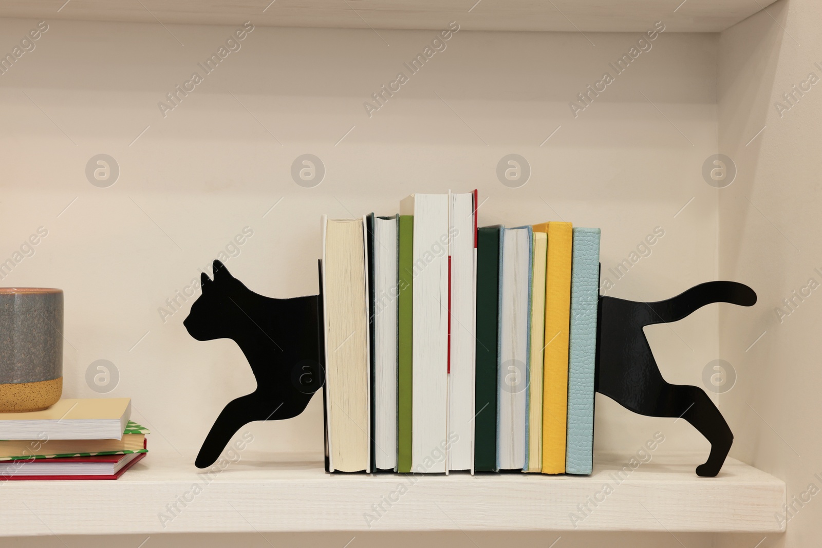 Photo of Decorative cat bookends with books on shelf indoors