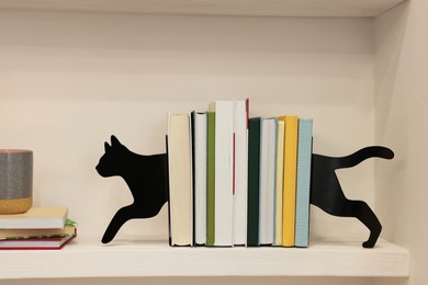 Photo of Decorative cat bookends with books on shelf indoors