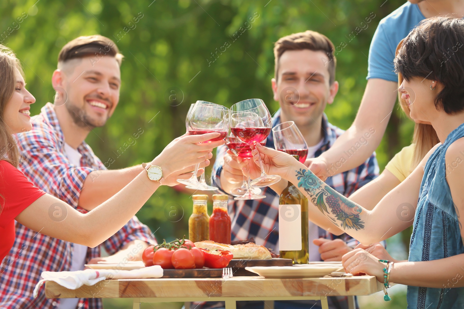 Photo of Young people with glasses of wine at table outdoors. Summer barbecue