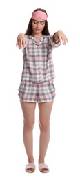 Young woman wearing pajamas, mask and slippers in sleepwalking state on white background
