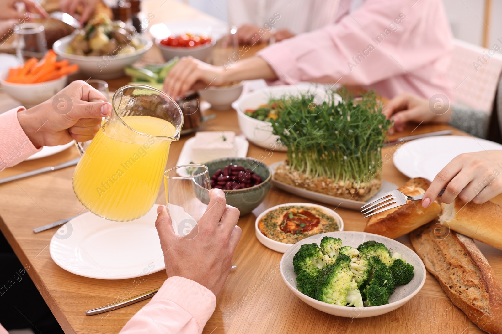 Photo of Friends eating vegetarian food at wooden table indoors, closeup