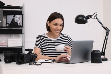 Photo of Young professional photographer with camera working on laptop in modern photo studio