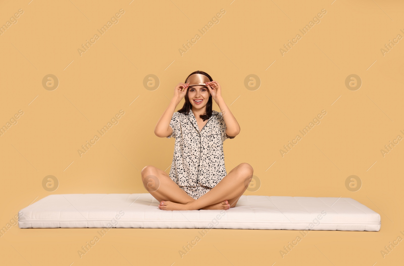 Photo of Woman in sleep mask on soft mattress against beige background