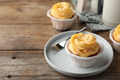 Photo of Tasty cupcakes with cream served on wooden table. Space for text