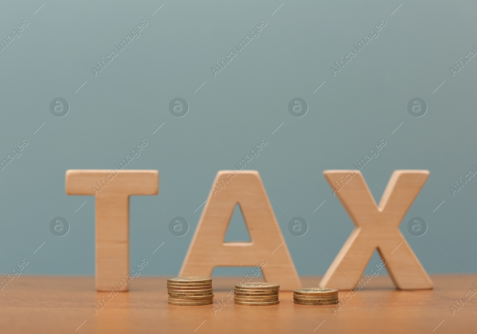 Photo of Word TAX and coins on table against color background