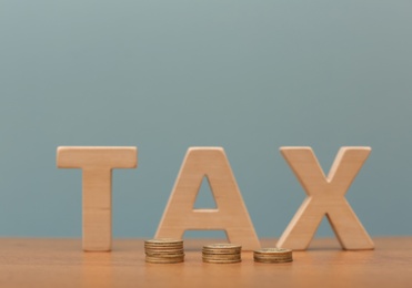 Photo of Word TAX and coins on table against color background