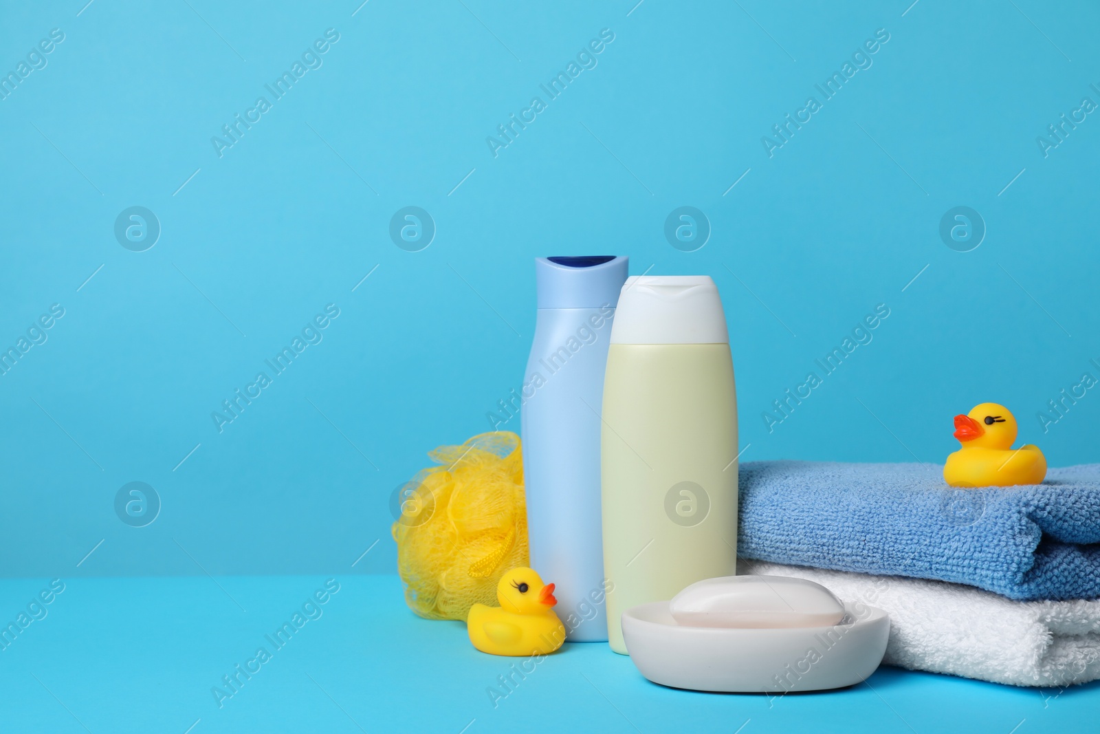 Photo of Baby cosmetic products, bath ducks, sponge and towels on light blue background. Space for text