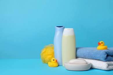 Photo of Baby cosmetic products, bath ducks, sponge and towels on light blue background. Space for text