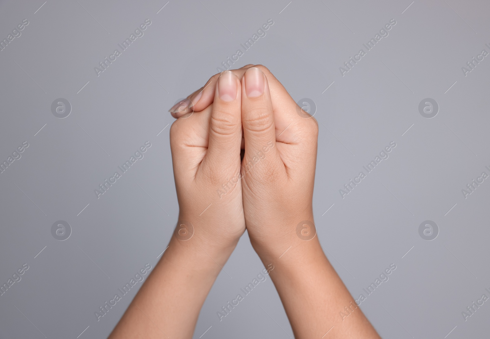 Photo of Woman with clasped hands while praying on light grey background, closeup