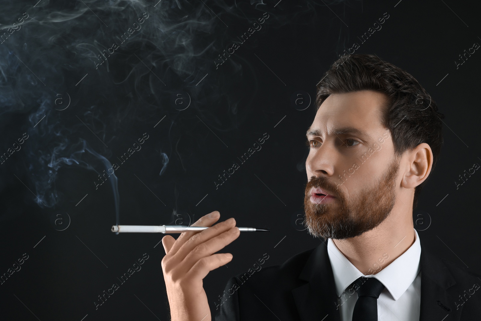 Photo of Man using long cigarette holder for smoking on black background