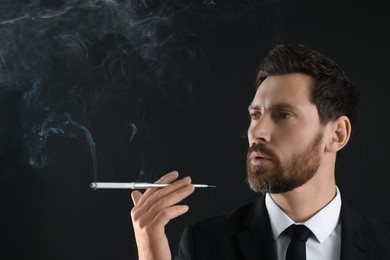 Man using long cigarette holder for smoking on black background